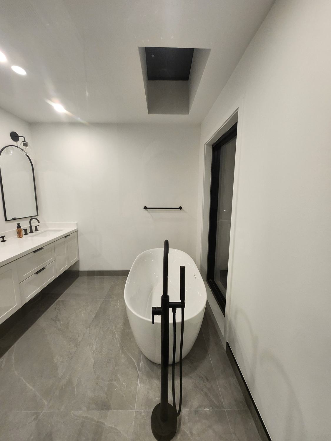 Bathroom with freestanding tub, matte black floor-mounted filler and arched mirror