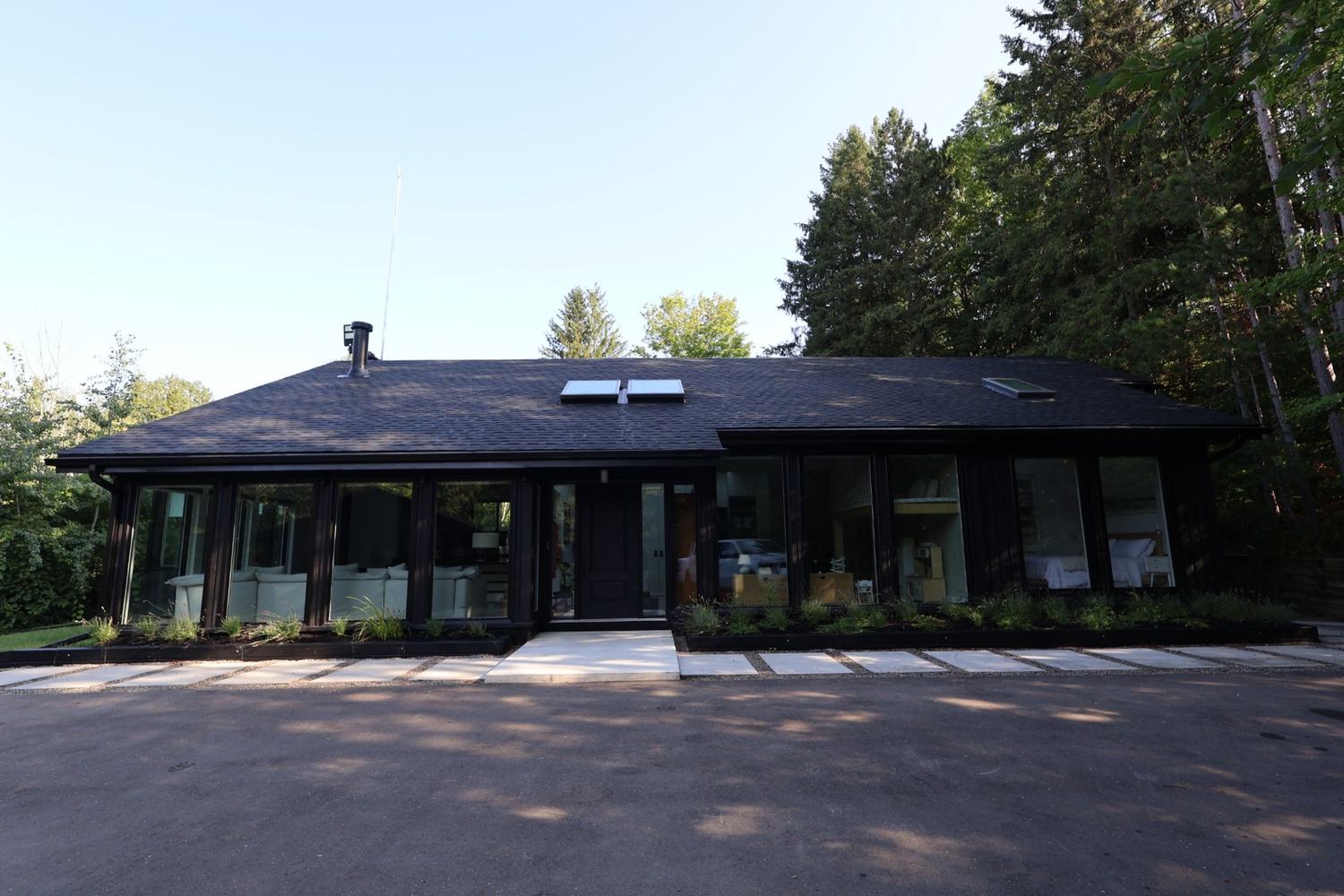 Long, low dark-clad home with a wall of windows facing the drive