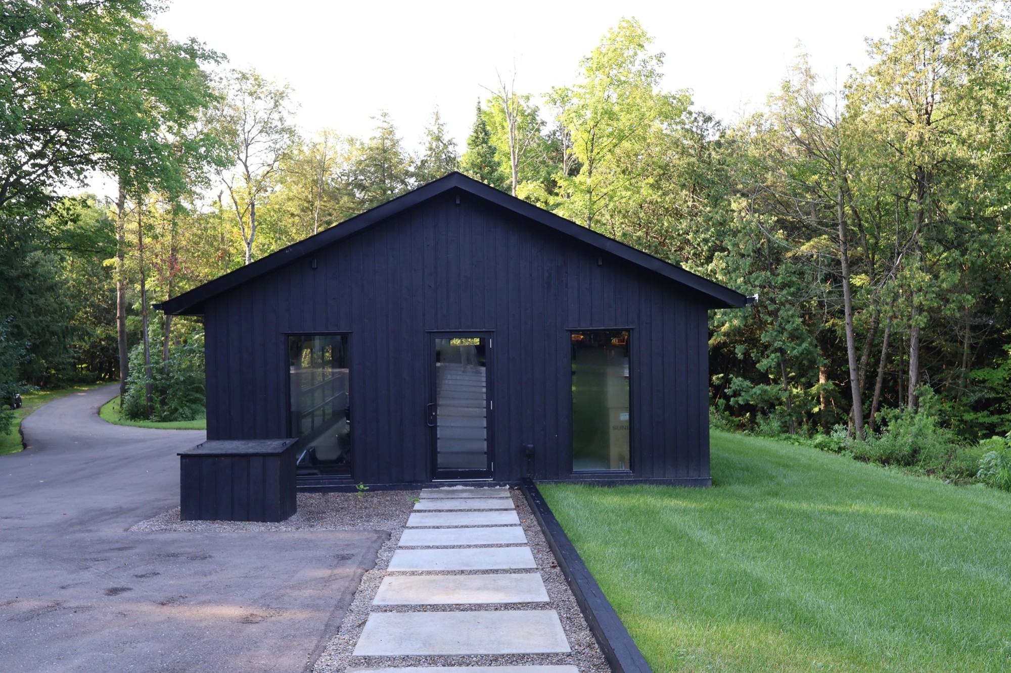 Dark board-and-batten home with large windows, set on a wooded lot