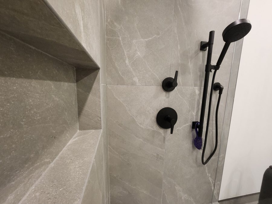 Shower wall in large-format grey porcelain with recessed niche and matte black fixtures